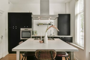 Şık ve çağdaş bir mutfak, parlak bir tasarım, siyah dolaplar, geniş bir masa ve doğal ışıkla güçlendirilmiş parlak bir atmosfer..