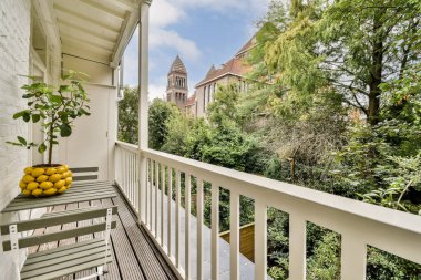 Bitkiler ve limonlarla süslenmiş güzel bir balkon, canlı bir yeşillik manzarası ve arka planda çarpıcı tarihi bir bina sunuyor..