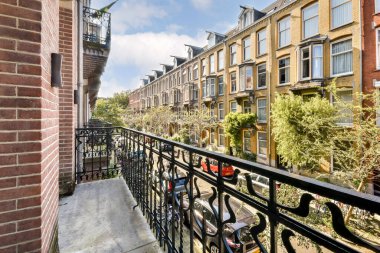 Ağaçlarla kaplı bir caddeye bakan bir balkondan manzara ve detaylı mimarisi olan zarif binalar, şehir hayatını gözler önüne seriyor..