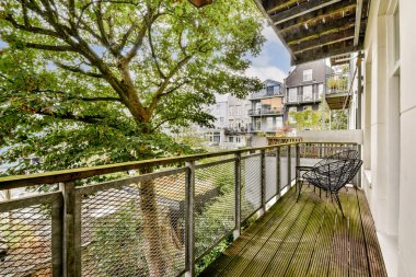 Ahşap döşeme, metal korkuluklar ve yakınlardaki ağaçlardan gelen yeşilliklerle dolu pitoresk bir balkon, dinlenmek için mükemmel bir açık hava alanı sunuyor..