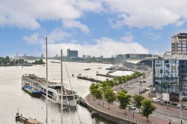 Canlı bir deniz manzarası modern binalar, tekneler ve hareketli bir nehir kenarı gezinti alanı. Ufuk çizgisi sakin suyla çelişiyor, şehir yaşamını güzel bir şekilde yakalıyor..