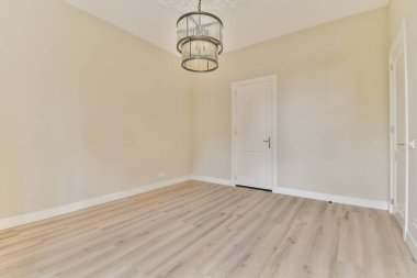 Geniş, minimalist bir oda. Açık renkli duvarlar, ahşap bir zemin ve şık bir avize. Huzurlu ve davetkar bir atmosfer yaratıyor..