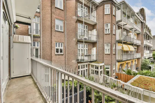 Modern bir apartman balkonundan manzaralı bir manzara klasik tuğla mimarisini ve aşağıdaki manzaralı bahçeleri sergiliyor, sakin bir kentsel atmosfer yaratıyor..