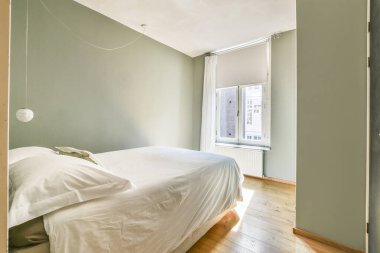 Pencereden süzülen, minimalist tasarım ve sıcak ahşap döşeme sergilenen yumuşak doğal ışık ile sakin bir yatak odası..