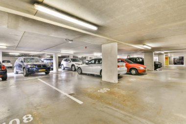 Geniş, modern bir yeraltı otoparkı. Temiz beton bir ortamda parlayan, park halindeki çeşitli arabaları gösteriyor..