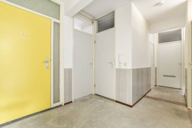 Yeni, modern bir koridor, parlak sarı bir kapı, minimal tasarım, ve temiz çizgiler, davetkar bir atmosfer yaratıyor..