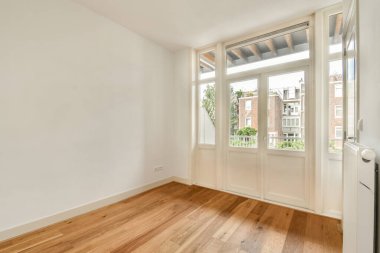 Geniş ve minimalist bir oda, geniş pencereli doğal ışık alan, ahşap zemin ve nötr duvarlar sergilenen, modern yaşam için ideal..