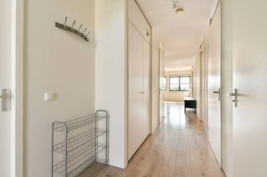 Geniş ve modern koridorda minimalist dekorlar, açık renkli duvarlar ve büyük pencerelerden gelen doğal ışık ile tamamlanmış ahşap döşemeler var..