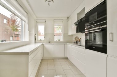 Beyaz dolap, minimalist bir tasarım ve doğal ışığın alanı zarifçe aydınlatmasına izin veren geniş pencereli gösterişli, modern bir mutfak..