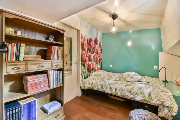 Parlak, davetkar bir yatak odası, çiçeklerle süslenmiş bir yatak odası, kitaplarla dolu ahşap bir raf, ve duvarlarda lale resimleri..