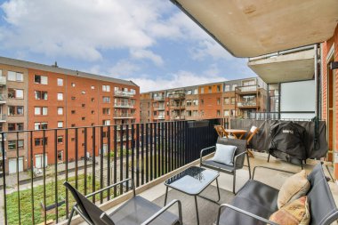 Modern mobilyaların ve tuğla bina kompleksinin olduğu geniş bir balkon, rahatlama ve açık havada yaşam için ideal..