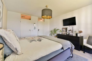 Konforlu oturma odasında modern mobilyalar, şık bir aydınlatma armatürü ve duvara monte edilmiş bir televizyon sergilenerek rahat ve şık bir ortam yaratılıyor..