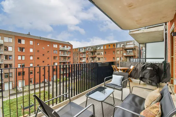 Modern mobilyaların ve tuğla bina kompleksinin olduğu geniş bir balkon, rahatlama ve açık havada yaşam için ideal..