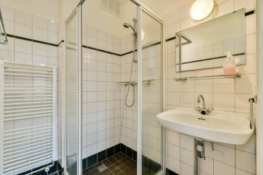 Çağdaş bir lavabo ile cam duş muhafazası sergilenen gösterişli, modern bir banyo. Tasarımda temiz çizgiler ve minimalist dekorlar yer alıyor..