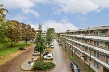 Yeşil ağaçlar, park edilmiş araçlar ve binalar boyunca iyi korunan bir yürüyüş yolunun yer aldığı modern yerleşim yerinin manzarası..