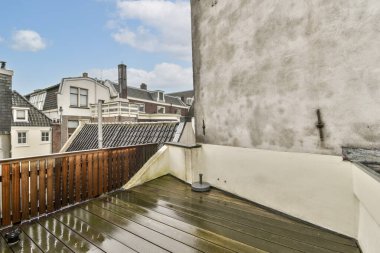 Çağdaş binaların arka planına karşı yağmura batırılmış ahşap bir güverte sergilenen şık bir şehir terası. Açık hava rahatlama ya da toplanma için ideal..