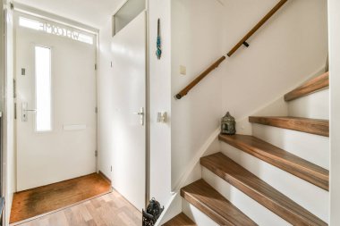 Parlak bir kapısı, ahşap merdivenleri ve minimalist dekoru olan modern bir giriş. Mekan davetkar ve şık, çağdaş bir ev için mükemmel..