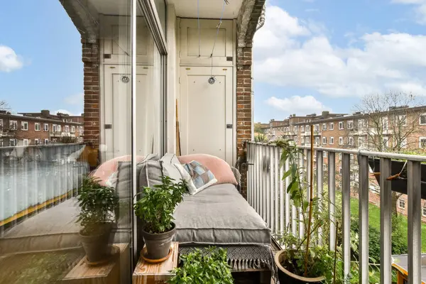 Yastıklı bir oturma alanı olan rahat bir balkon. Bitkilerle süslenmiş ve canlı bir şehir manzarasını yansıtan bir manzara..