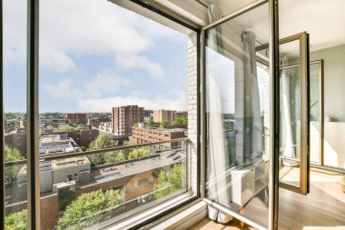 Geniş, modern bir daire, arka planda yeşillik ve şehir manzarasıyla geniş pencerelerden çarpıcı bir şehir manzarası sergiliyor..