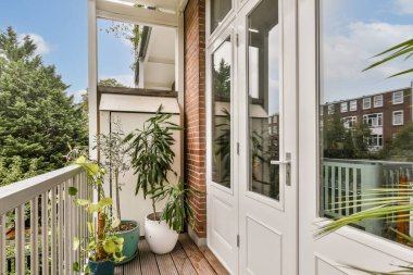 Bereketli yeşil bitkiler ve bol doğal ışık içeren modern bir balkon dinlenmek ve keyif almak için sakin bir açık hava alanı sağlar..