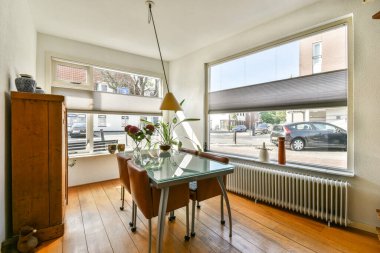 Cam bir masa, ahşap döşeme ve geniş pencerelerden yayılan bol miktarda doğal ışığın bulunduğu şık bir yemek salonu. Minimalist dekor alanı güçlendirir.