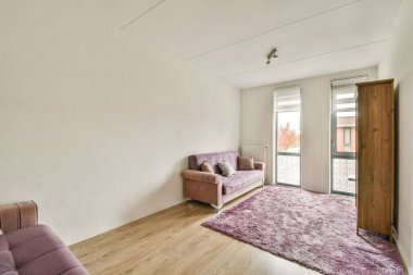 Rahat bir kanepe ve geniş pencereleri olan şık bir minimalist iç mekan, doğal ışığın boşluğu doldurmasına ve sıcak bir ortam yaratmasına izin veriyor..