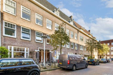 İçinde tuğla bina, büyük pencereler, yeşillik ve park edilmiş araçlar bulunan çağdaş şehir mimarisi. Şehir ortamında davetkar bir sokak sahnesi.