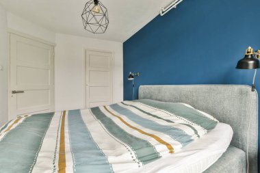 Zarif modern yatak odası çizgili, minimalist dekorlu rahat bir yatak odası, ve şık bir aydınlatma armatürü, huzurlu bir atmosfer yaratıyor..