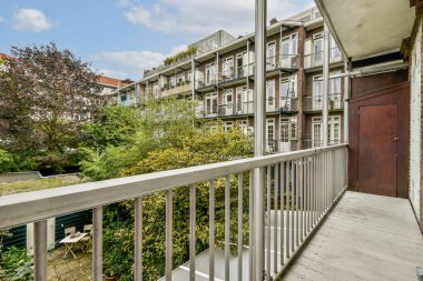 Sakin bir balkon manzarası şehir mimarisi ve yemyeşil bir karışım sergiliyor, rahatlamayı ve şehir yaşamının ortasındaki doğayla bağlantıyı teşvik ediyor..