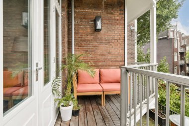 Pembe bir kanepe ve saksı bitkilerinin bulunduğu büyüleyici bir balkon sahnesi, kırsal tuğla bir duvara dayanır, rahatlama ve açık hava keyfi için idealdir..