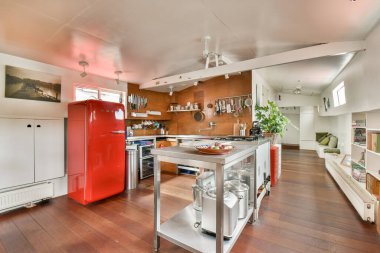 Canlı kırmızı bir buzdolabı ve sıcak, modern bir atmosfer yaratan ahşap aksanlı bir mutfak. Yemek ve toplanma için mükemmel..