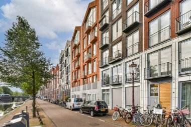 Çağdaş konut binaları, sakin bir kanalın yanında, ağaçlar ve park edilmiş bisikletlerle hayat dolu sokak yaşamını güçlendiriyor..