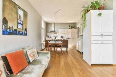 Kanepenin üzerinde renkli yastıklar, ahşap döşemeler ve sanatsal dekorasyonla tamamlanmış açık mutfak eşyaları olan şık bir oturma odası..