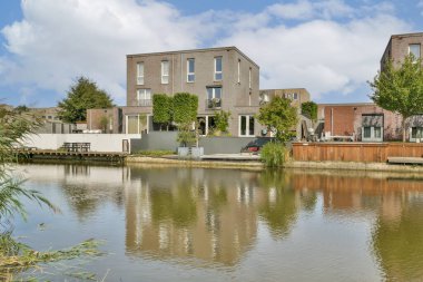 Çağdaş bir yerleşim yeri çevresi yeşilliklerle çevrili ve modern mimari tasarım sergilenen sakin bir su kütlesine yansıyor..