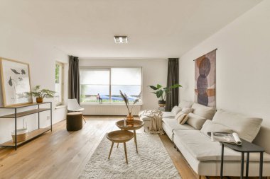 Tarafsız tonlara, rahat bir kanepeye, dekoratif sanata ve geniş pencerelerden yayılan doğal ışığa sahip modern bir oturma odası, huzurlu bir atmosfer yaratıyor..