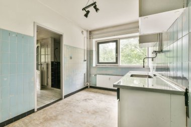 Açık mavi duvarlar, büyük pencereler ve işlevsel dolaplarla dolu basit ve ferah bir mutfak, temiz ve parlak bir yemek alanı yaratıyor..