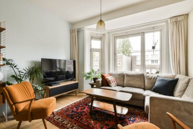 Rahat bir kanepe, bir sehpa ve iç mekan bitkileri ve canlı dekorlarla süslenmiş büyük bir televizyonu olan şık bir oturma odası..