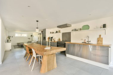 Geniş ve çağdaş bir mutfak. Ahşap bir yemek masası, paslanmaz çelik aletler ve modern yaşam için mükemmel bir tasarım..