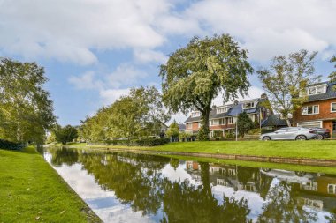 Sakin bir nehir manzarası, yakınlardaki büyüleyici evlerle tamamlanmış sakin bir su yolu oluşturan ağaçlar. Açık gökyüzü manzarayı güzelleştirir..