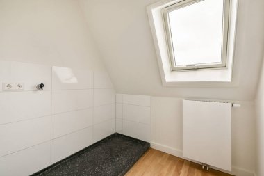 Bu resimde, eğimli tavanı, beyaz fayansları ve parlak ısıtması olan çağdaş bir banyo var. Minimalist tasarım ışığı ve uzayı vurgular..