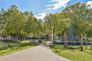 Canlı yeşil ağaçlar ve gökyüzünde neşeli bulutlarla çevrili dolambaçlı bir patikadan oluşan sakin bir park sahnesi rahatlama ve rahatlamaya davetiye çıkarıyor..