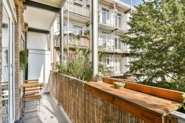 Parlak ve ferah bir balkon. Saksı bitkileri ve ahşap koltuklar var. Rahatlamak için ideal. Sahne, canlı yeşilliklerle huzurlu bir açık alan yakalıyor..