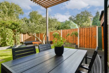 Yeşillik ve ahşap çitlerle çevrili siyah bir masa ve sandalyelerin bulunduğu şık bir açık hava yemek alanı, rahatlama ve toplanma için mükemmel..