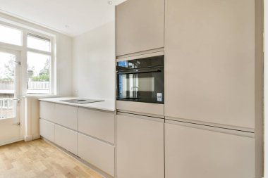 Gri dolaplar, entegre aletler ve doğal ışığa izin veren büyük pencerelerin yer aldığı zarif ve şık bir modern mutfak..