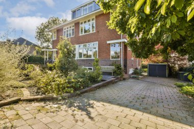 Canlı yeşillikler ve bakımlı bir bahçeyle çevrili tuğladan bir cepheye sahip güzel bir ev, davetkar görünümünü artırıyor..