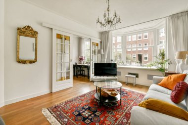 Şık bir oturma odası şık bir kanepe dekoratif yastıklar ve eski bir halı. Doğal ışık geniş pencerelerden süzülerek sıcak atmosferi arttırır..