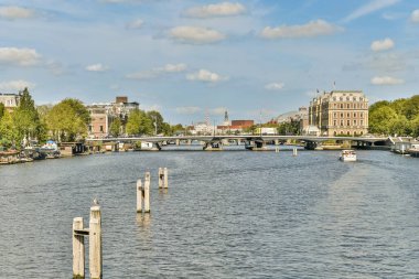 Köprülerin, teknelerin ve yemyeşil yeşilliklerin sergilendiği pitoresk bir nehir manzarası, kentsel doğanın güzelliğini yansıtıyor..