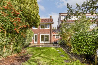 Bu sakin bahçe düzeninde iki katlı bir ev var. Yeşillik, bakımlı çimenler ve canlı bitki örtüsüyle huzurlu bir yerleşim ortamı yaratıyor..