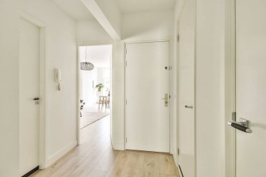 Beyaz duvarları ve ahşap döşemeleri olan, doğal ışığı uzaya davet eden modern minimalist bir estetiği gösteren parlak ve havadar bir koridor..