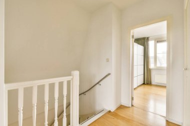 Ahşap döşeme ve modern dekorun yer aldığı temiz ve iyi aydınlatılmış bir koridor. Büyük pencereleri ve şık perdeleri olan parlak bir odaya açılıyor..
